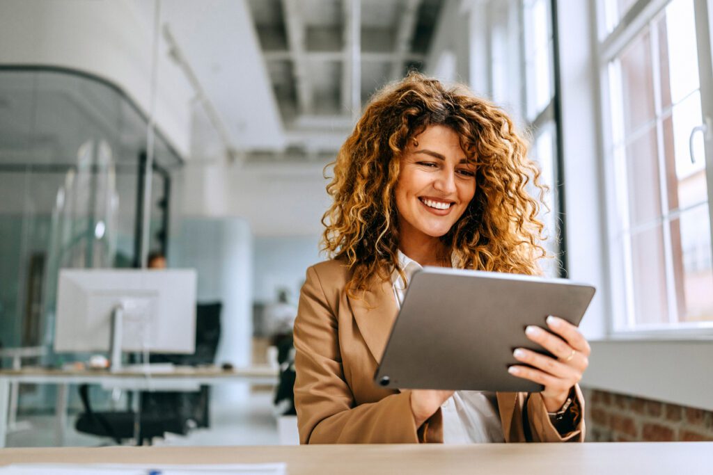 Smiling businesswoman reading Athrú Insights & News on a tablet in a bright office